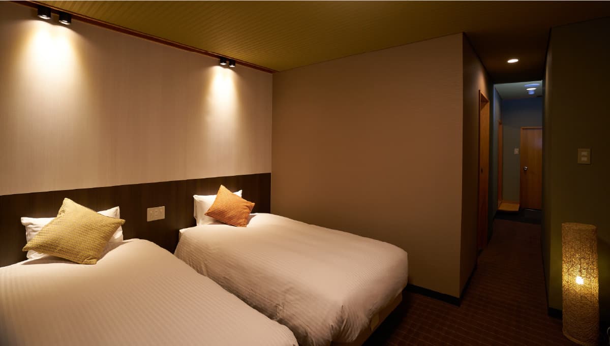 Modern twin-bed guest room with low lighting and warm wood tones at Meitoya So in Zao Onsen