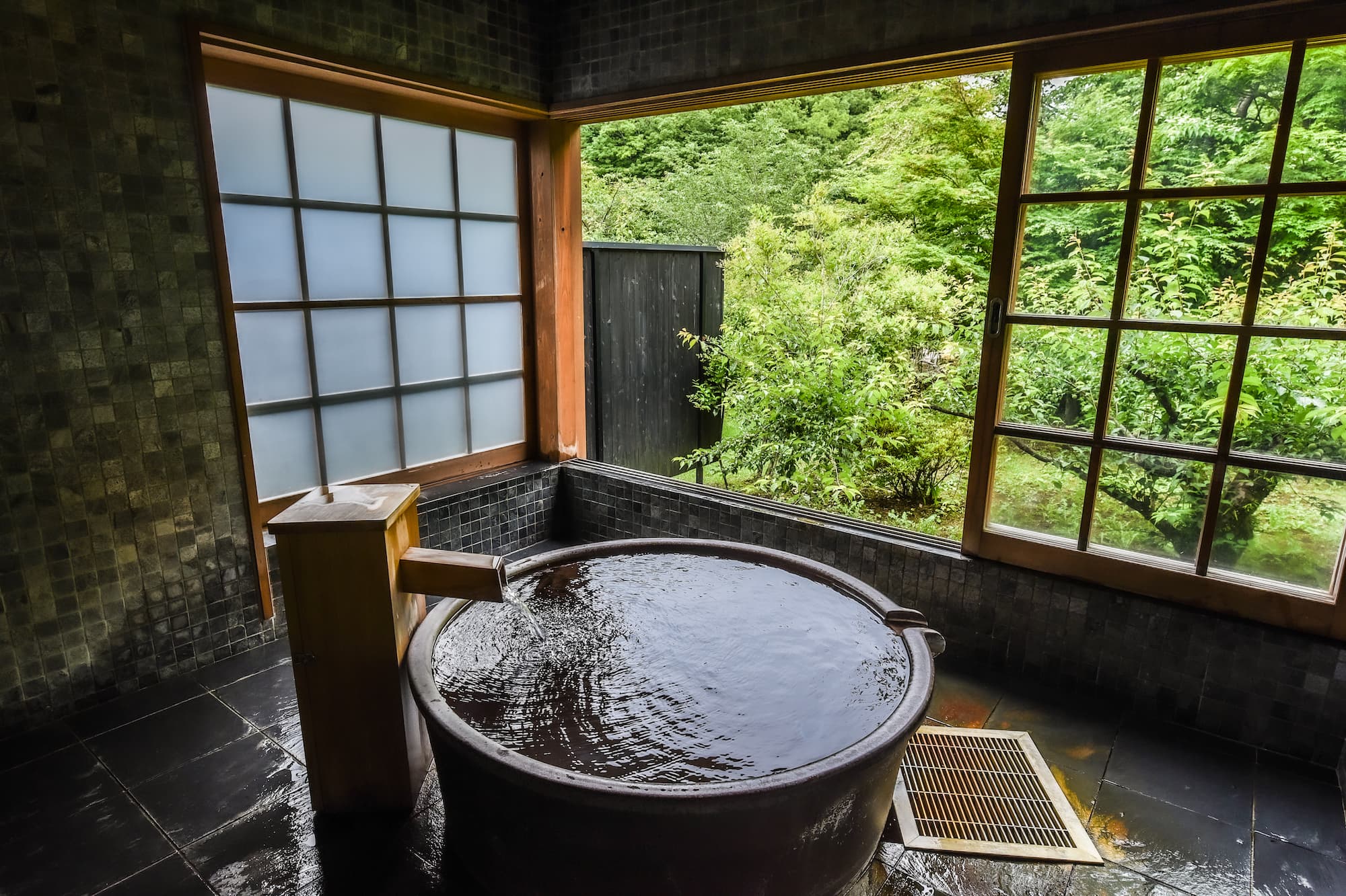 Private in-room open-air bath with a round stone tub looking out onto forest greenery