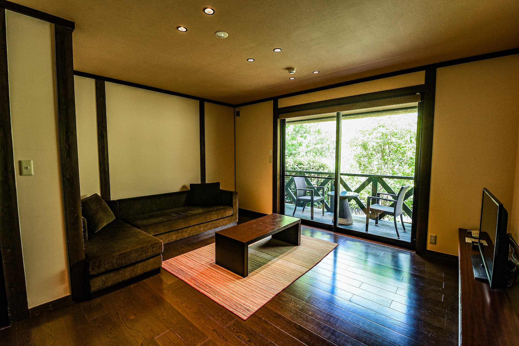 Guest room sitting area with rattan chairs and a low table opening onto a forest-view terrace