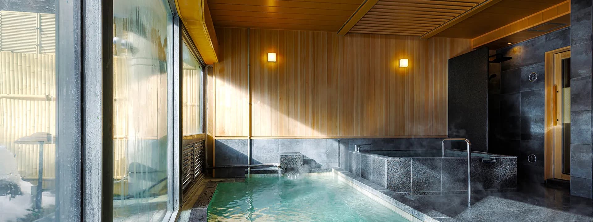 Indoor stone-and-wood public bath with large windows letting in soft daylight at Oku Nikko Mori no Hotel