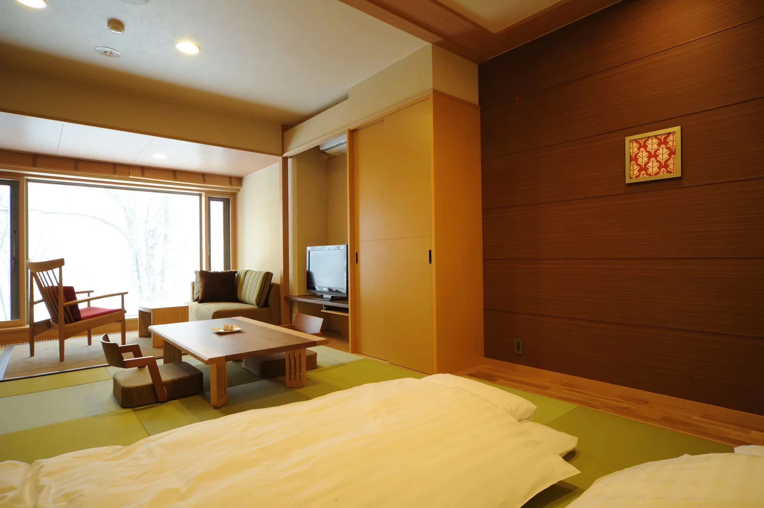Spacious tatami guest room with futon bedding laid out and a forest-view window at Oku Nikko Mori no Hotel