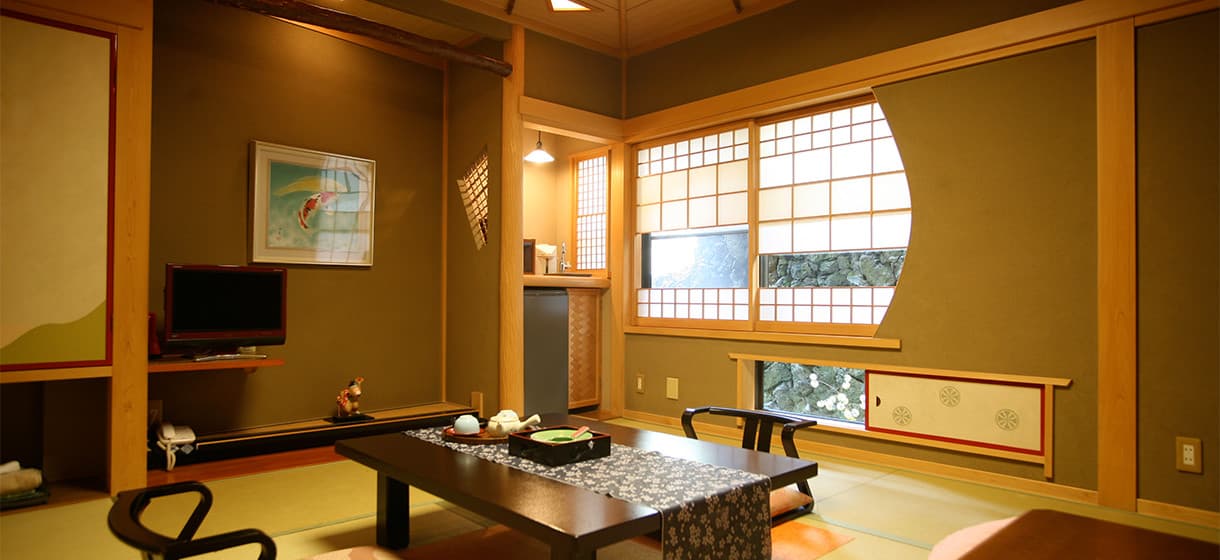 Japanese-style guest room at Morizuya with sunken sitting area, koi artwork and rounded shoji window overlooking greenery