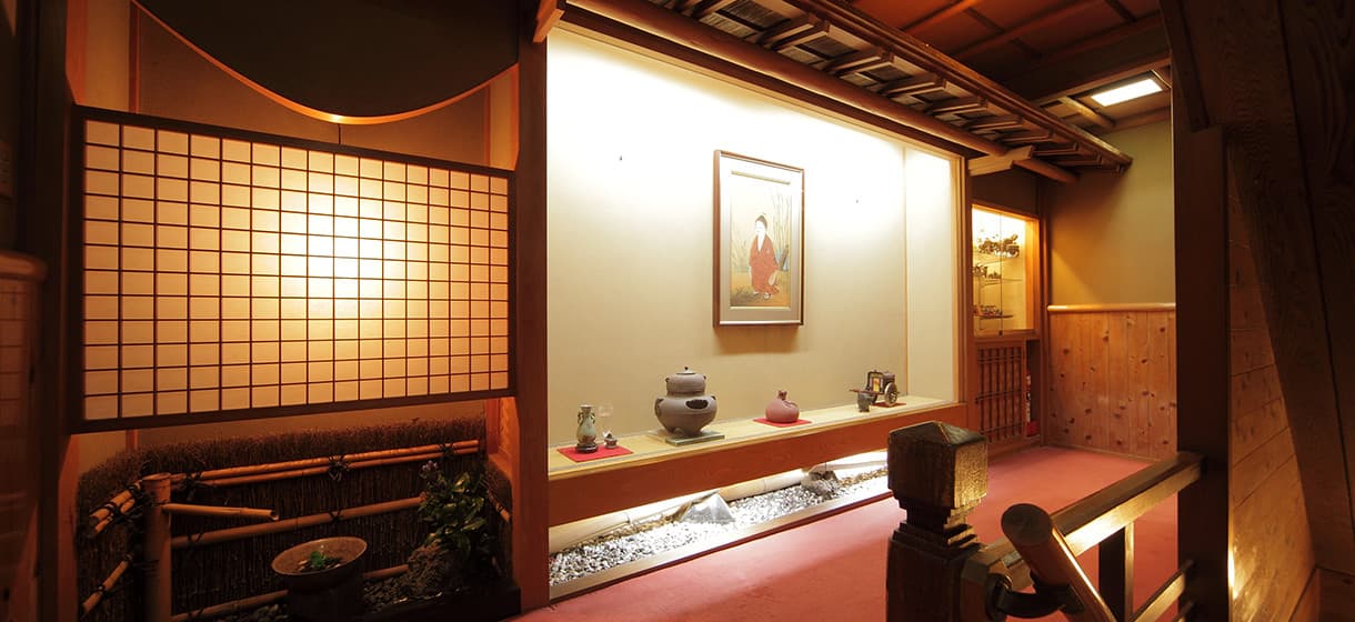 Hallway and tokonoma alcove at Morizuya with framed bijin-ga painting, tea utensils and warm lantern lighting