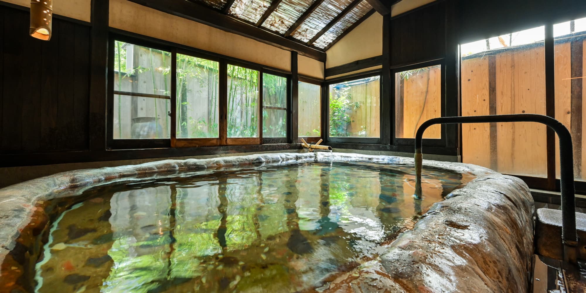 Indoor wooden hot-spring bath at Nansuikaku with windows overlooking a bamboo garden