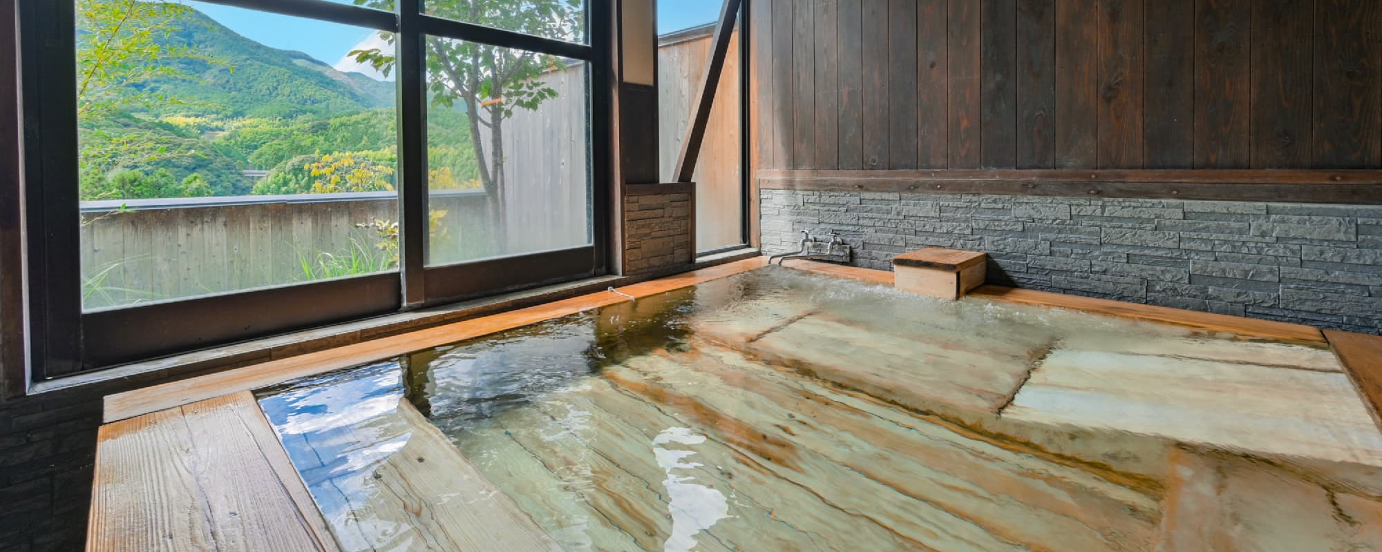 Stone hot-spring bath at Nansuikaku with a picture window framing the surrounding mountains