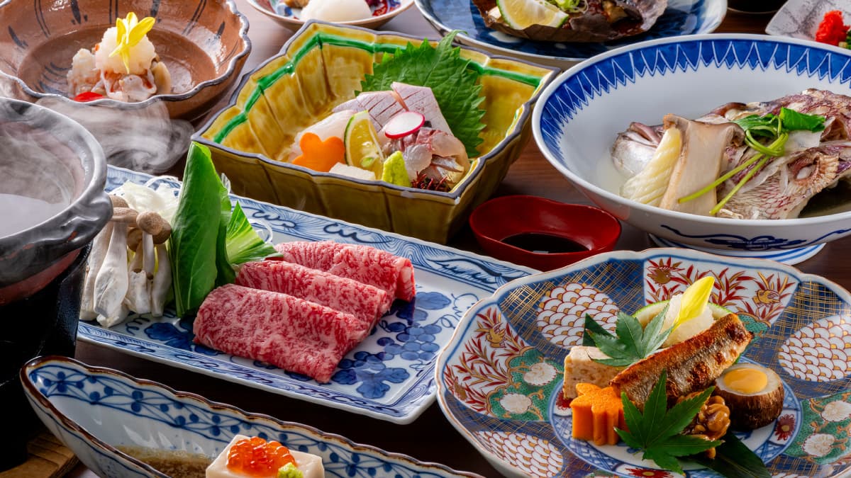 Kaiseki spread of marbled wagyu beef, sashimi and grilled fish on patterned porcelain dishes, Okamotoya Ryokan, Myoban Onsen, Beppu