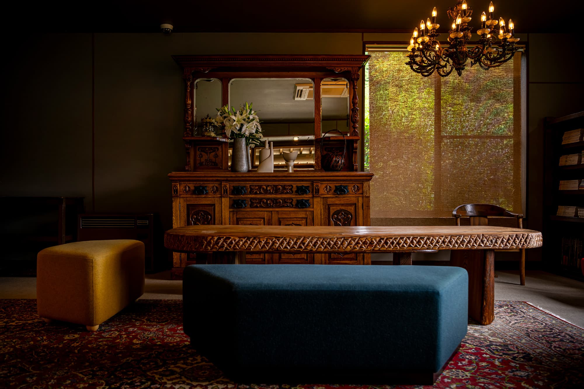 Antique-furnished lounge with carved wooden cabinet, ornate chandelier and woven blinds in dim warm light, Okamotoya Ryokan, Myoban Onsen, Beppu