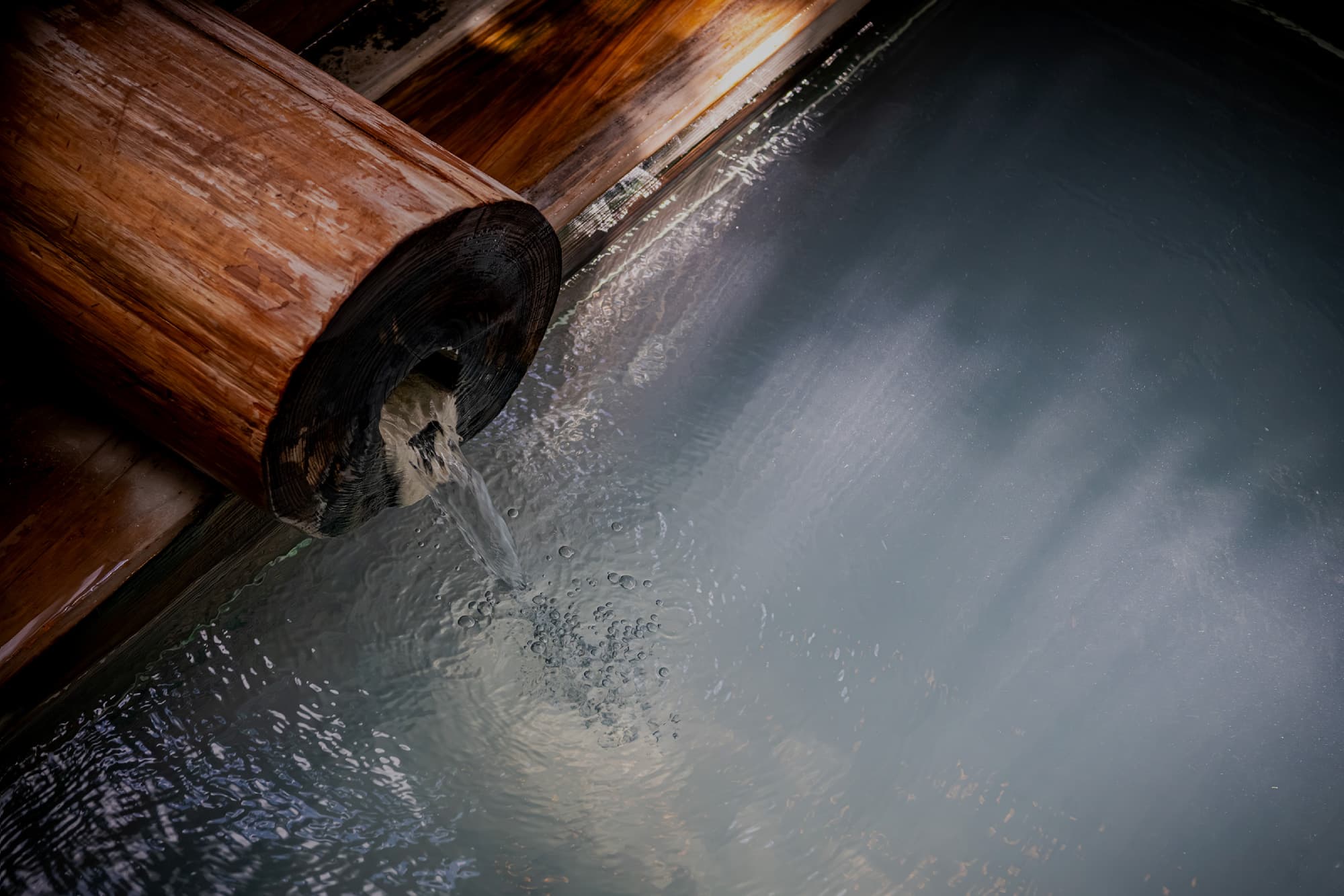 Hot spring water streaming from a hollowed wooden spout into a steaming milky bath, Okamotoya Ryokan, Myoban Onsen, Beppu