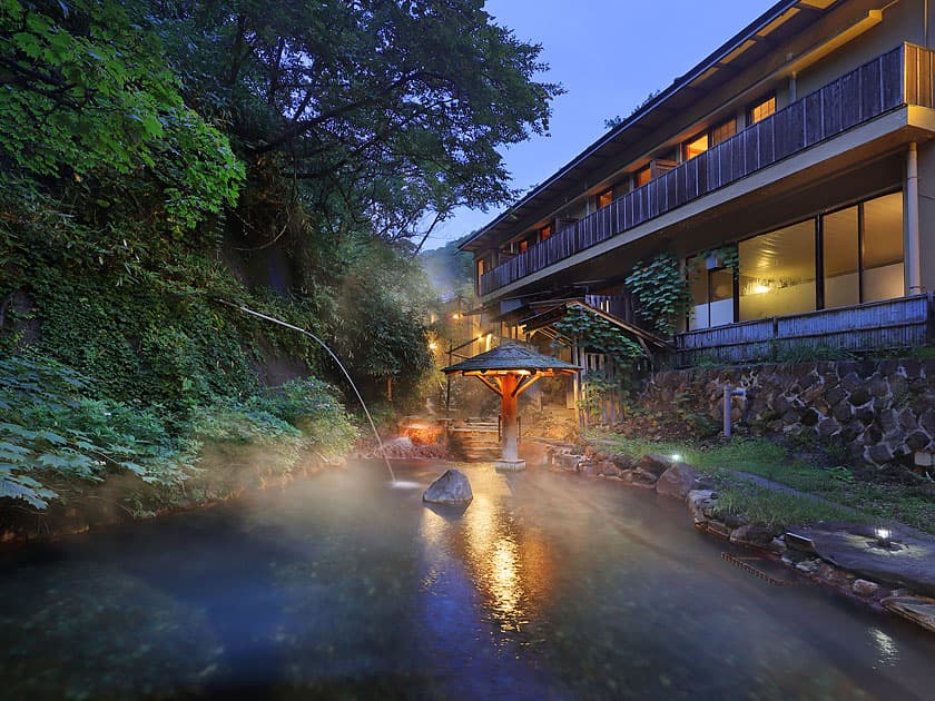 Natural riverbed open-air hot-spring bath steaming beside the inn at dusk