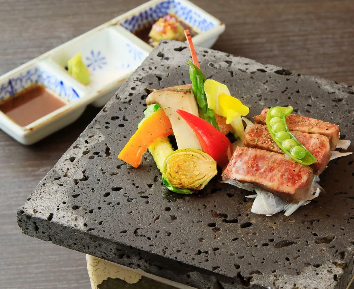 Grilled wagyu beef and seasonal vegetables served on a black lava stone plate at Fuji Onsenji Yumedono