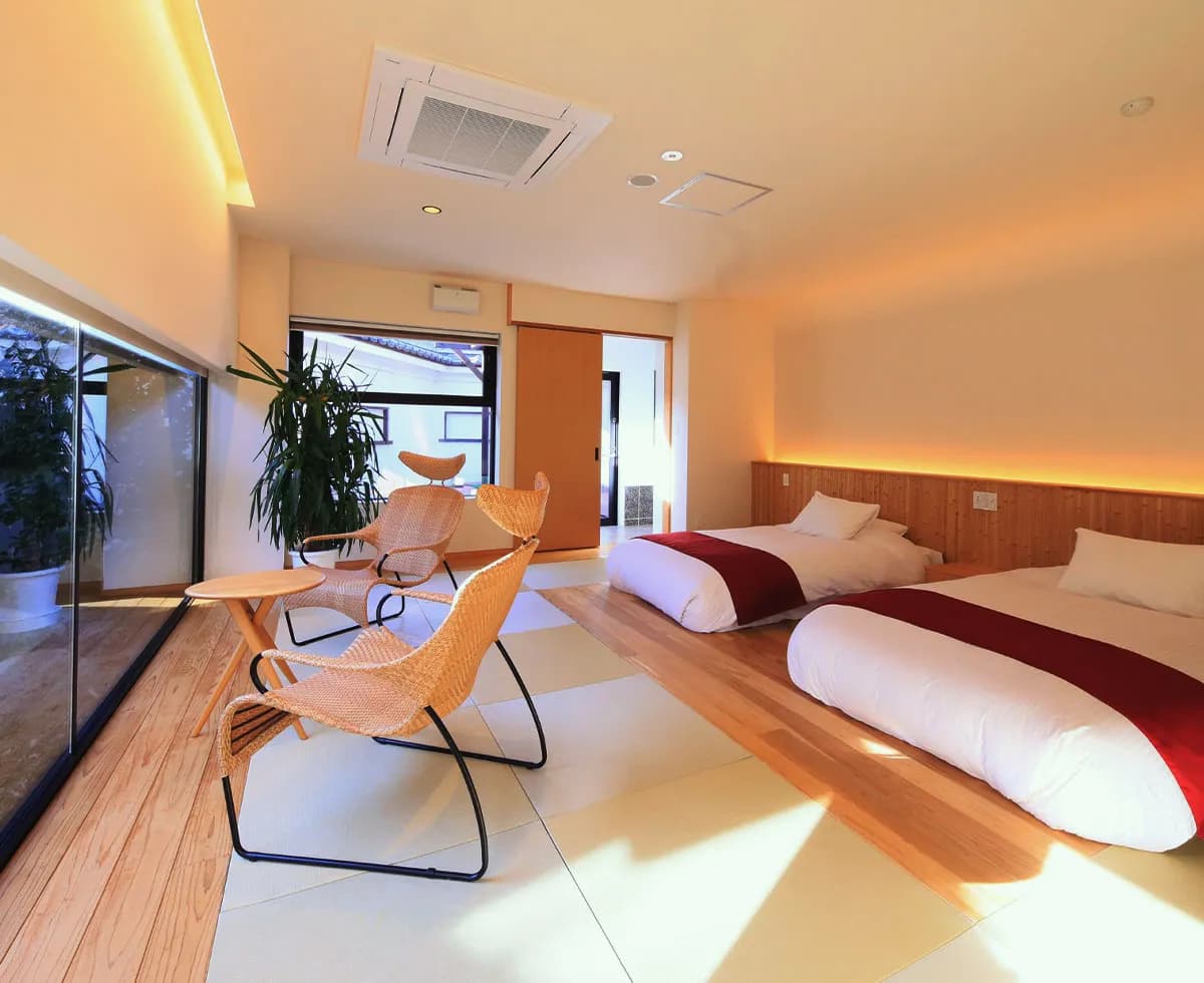 Bright modern guest room at Fuji Onsenji Yumedono with twin low beds, rattan lounge chairs and a tatami-and-wood floor