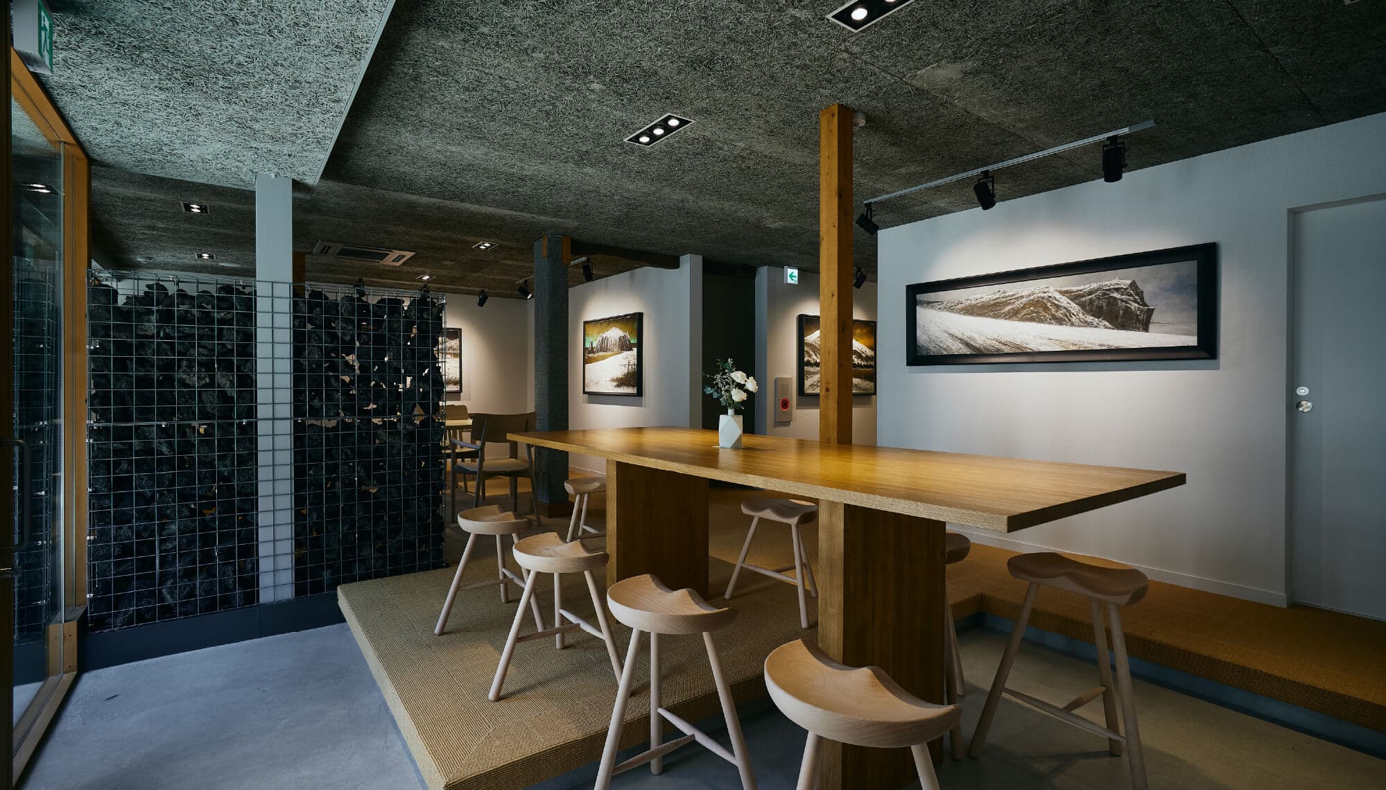 Gallery lounge at Tsuchiya with a long wooden communal table, low stools and framed landscape artworks