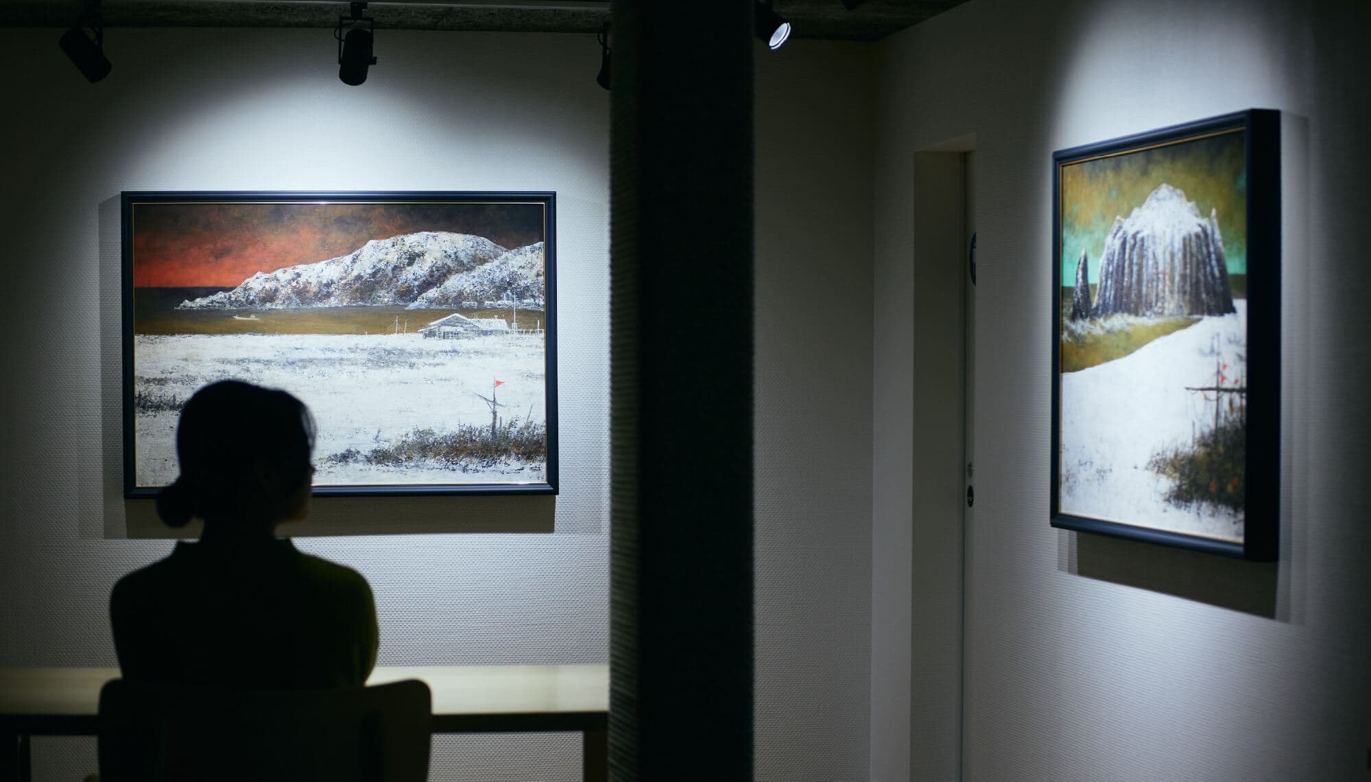 Interior art gallery space at Tsuchiya with spotlit framed paintings and a seated guest viewing the works