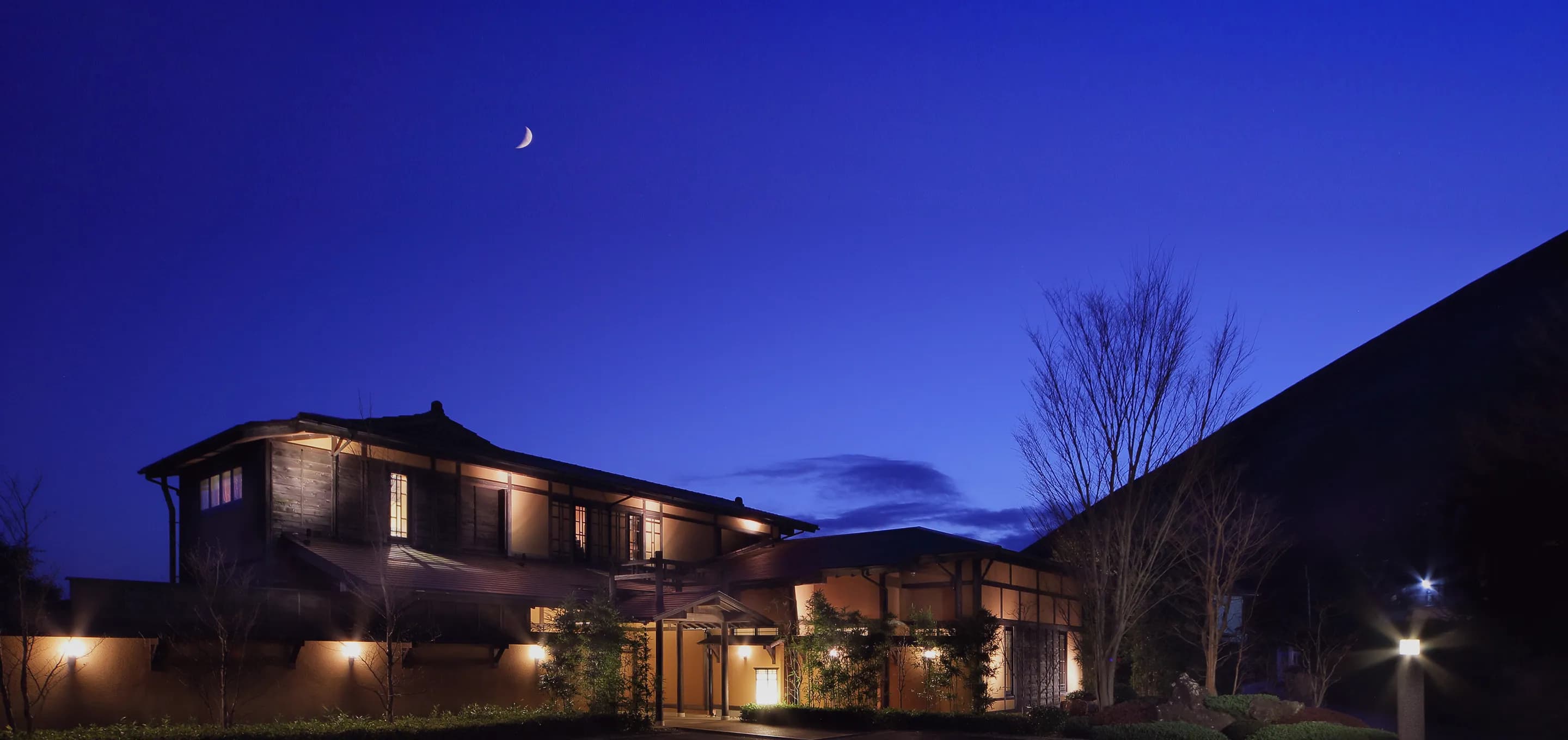 Oyado Uchiyama traditional Japanese inn building illuminated at twilight under a crescent moon in Izu
