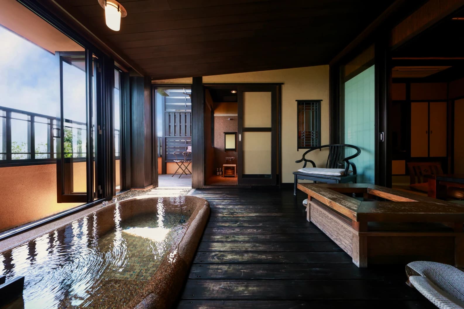 Spacious guest room interior at Oyado Uchiyama with a stone soaking bath, dark wood floor and terrace beyond
