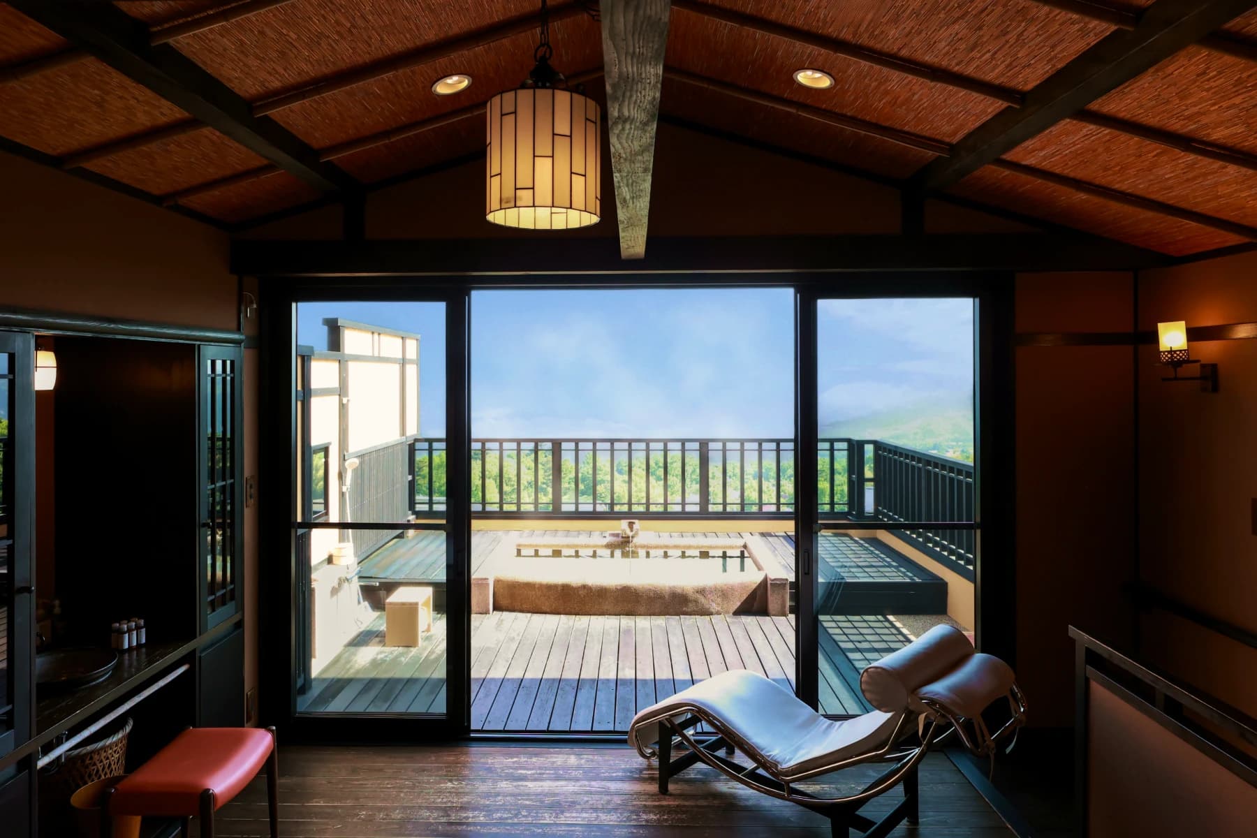 Tsuki guest room interior at Oyado Uchiyama with lounge chair and sliding doors opening to a terrace bath and green hillside view