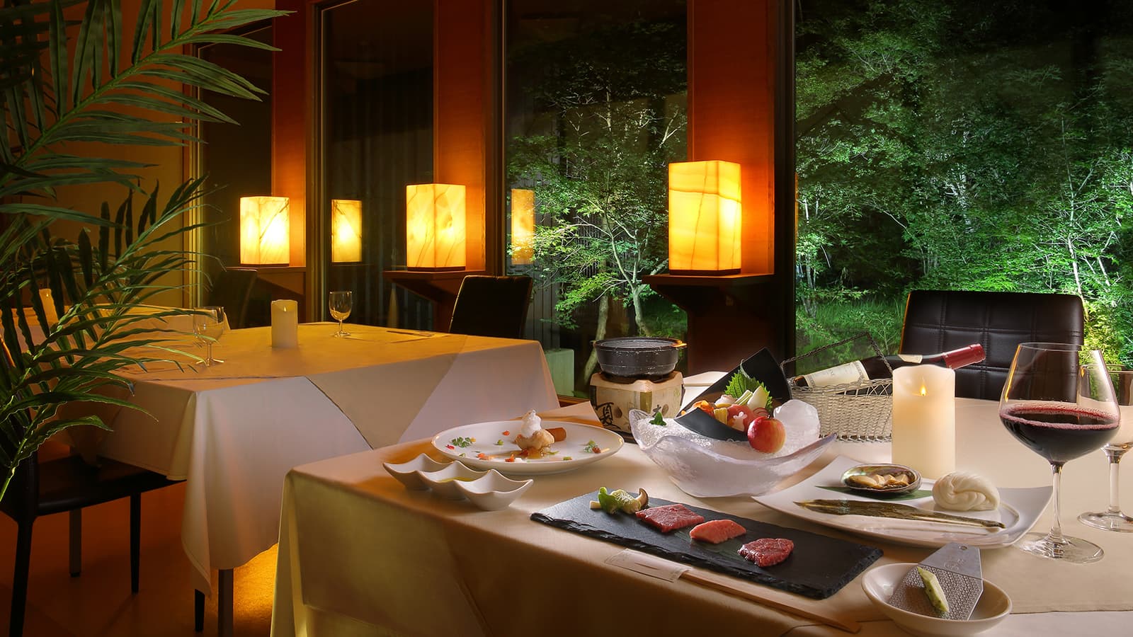 Candlelit dining table set with kaiseki courses and wine beside lantern-lined windows over the forest at Ryu Resort and Spa