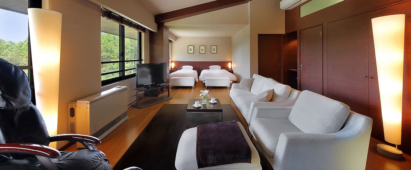Spacious twin guest room with white sofa lounge area, low table and forest-facing windows at Ryu Resort and Spa