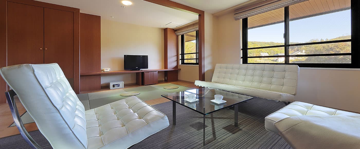 Modern Japanese-style guest room with white leather lounge seating, glass table and mountain view at Ryu Resort and Spa