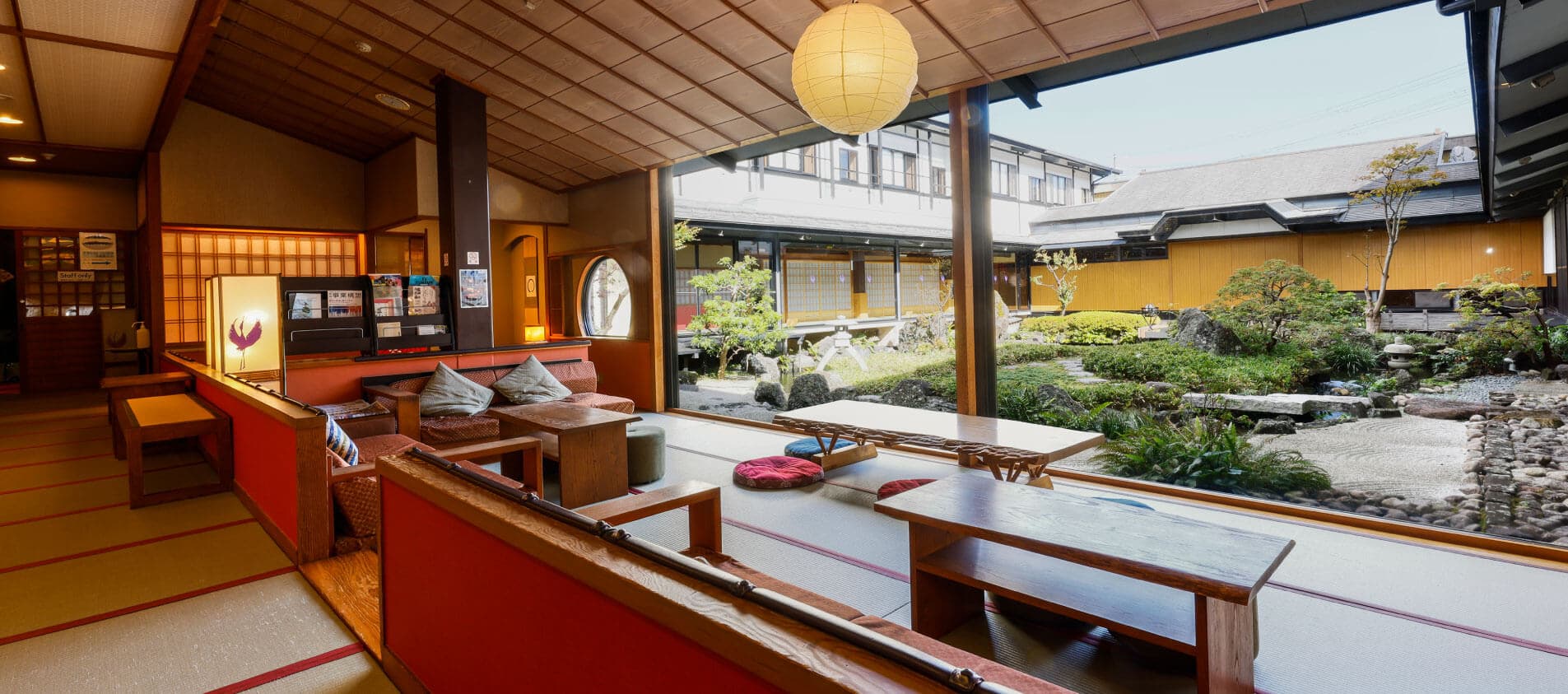 Tatami lobby lounge with low tables and paper lantern opening onto a landscaped inner garden, Onishiya Suishoen, Kinosaki Onsen