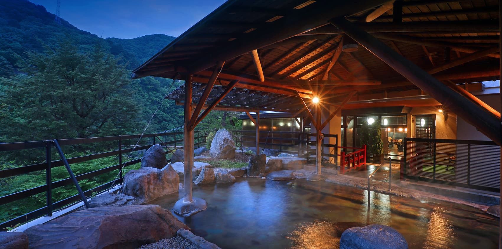 Covered rotenburo outdoor onsen at dusk with stone bath and forested gorge view at Hotel Sunshine Kinugawa, Nikko