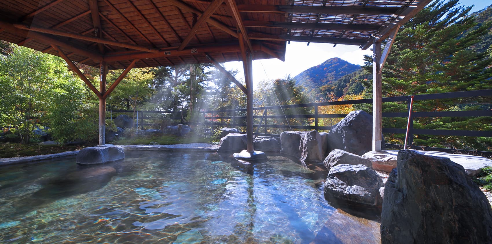 Open-air rotenburo hot spring bath with rising steam overlooking autumn-colored mountains at Hotel Sunshine Kinugawa, Kinugawa Onsen