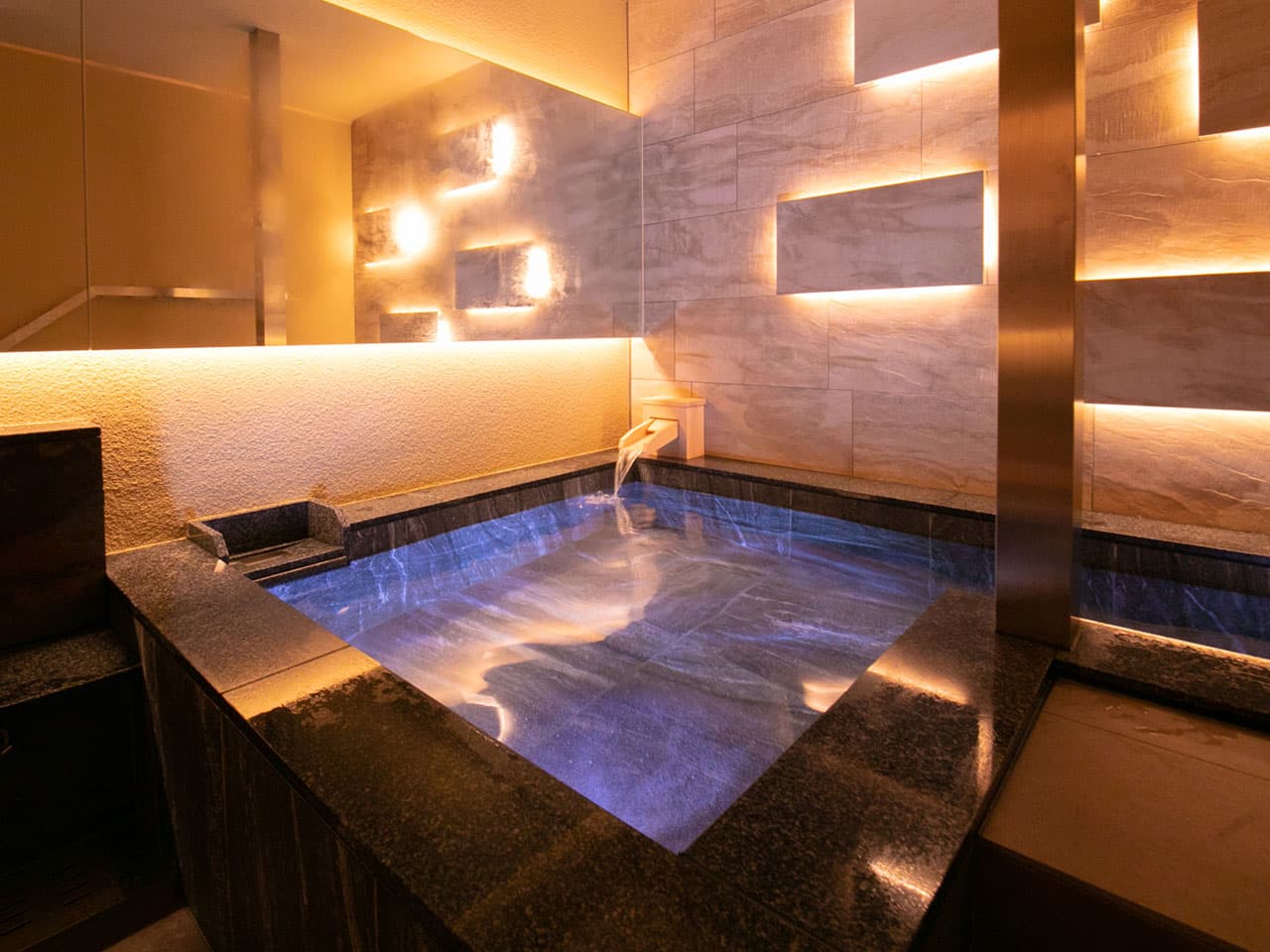Illuminated private suite bath at Tokitotoki with marble walls and a wooden water spout