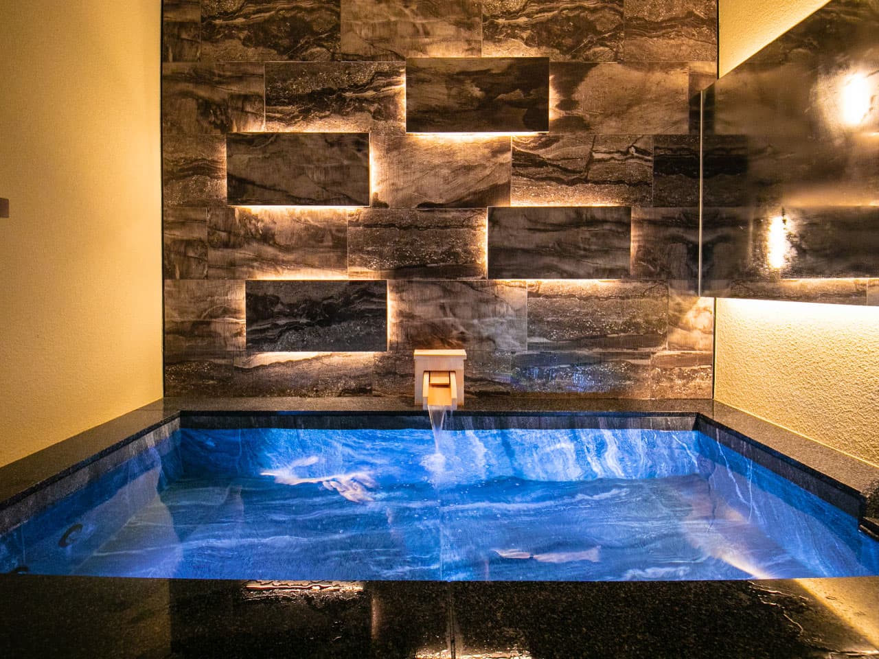 Second private suite bath at Tokitotoki glowing blue against a dark stone feature wall