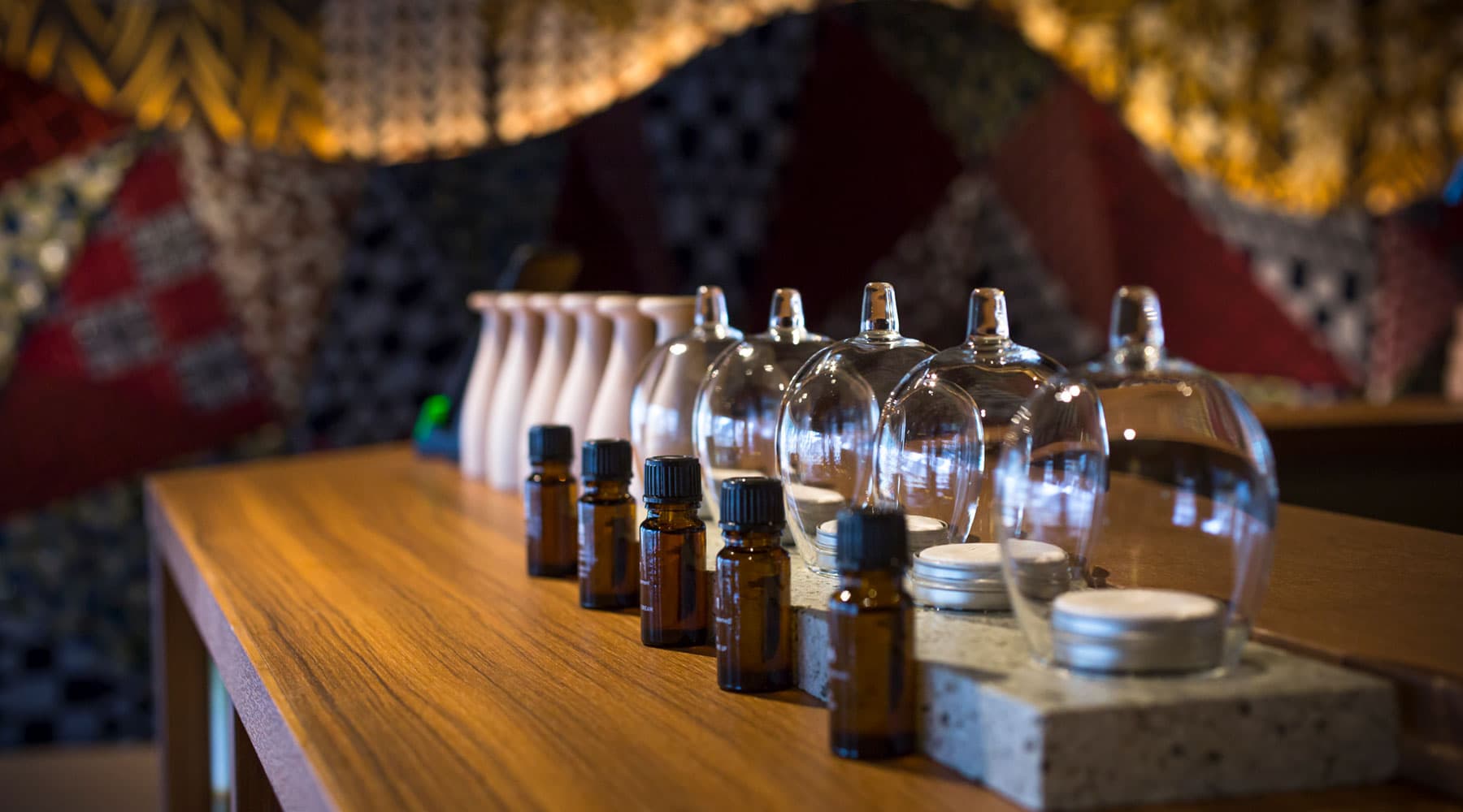 Aromatherapy oils and glass cups on a wooden shelf against a textile wall at Tokitotoki
