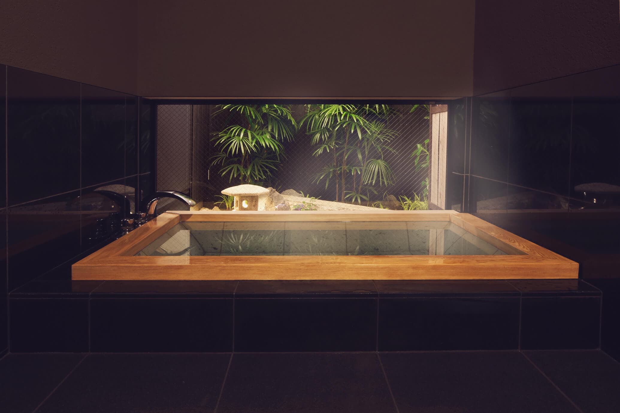 Indoor cypress-framed soaking bath looking onto a lantern-lit bamboo garden at The Edo Sakura, Tokyo