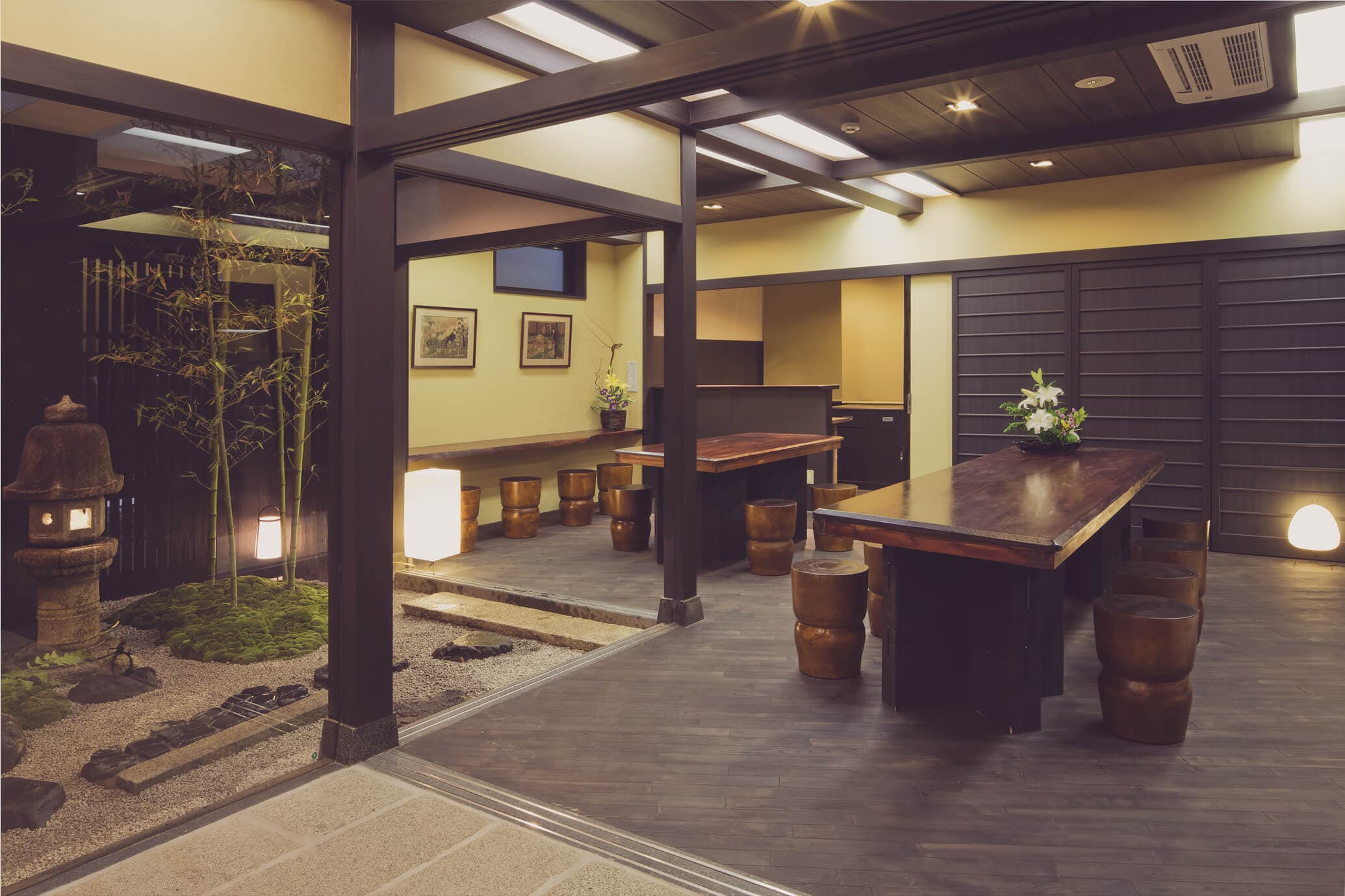Communal lounge with live-edge wood tables and drum stools beside an interior bamboo garden at The Edo Sakura, Tokyo