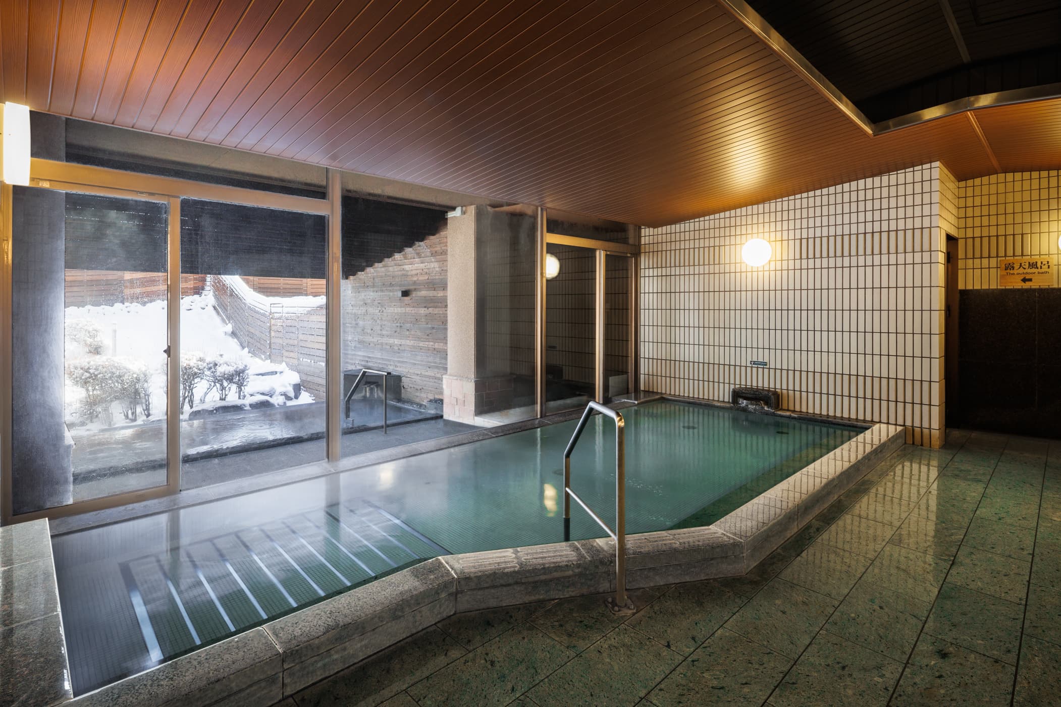 Indoor hot spring bath at Hakuba Tokyu Hotel with stone surround and a window framing the snowy outdoor garden