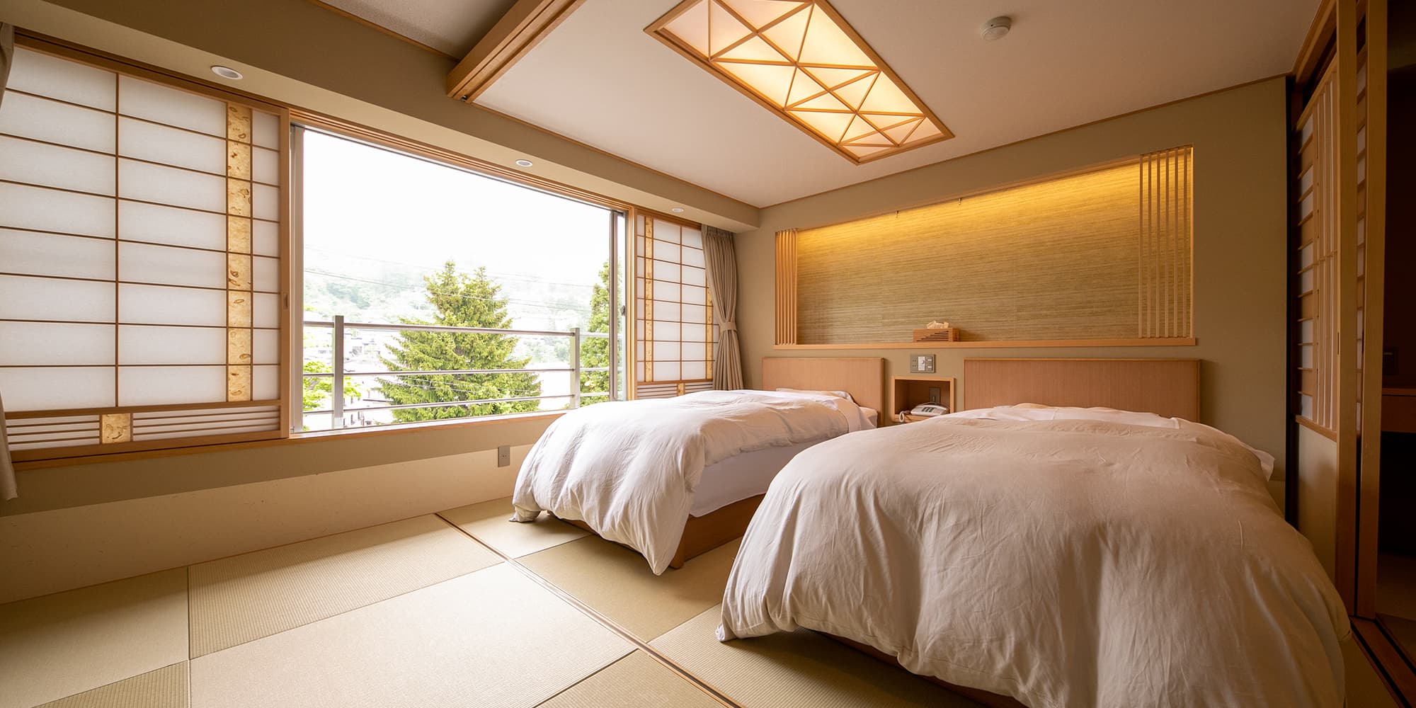 Japanese-Western guest room with twin beds on tatami flooring and shoji screens framing a mountain view