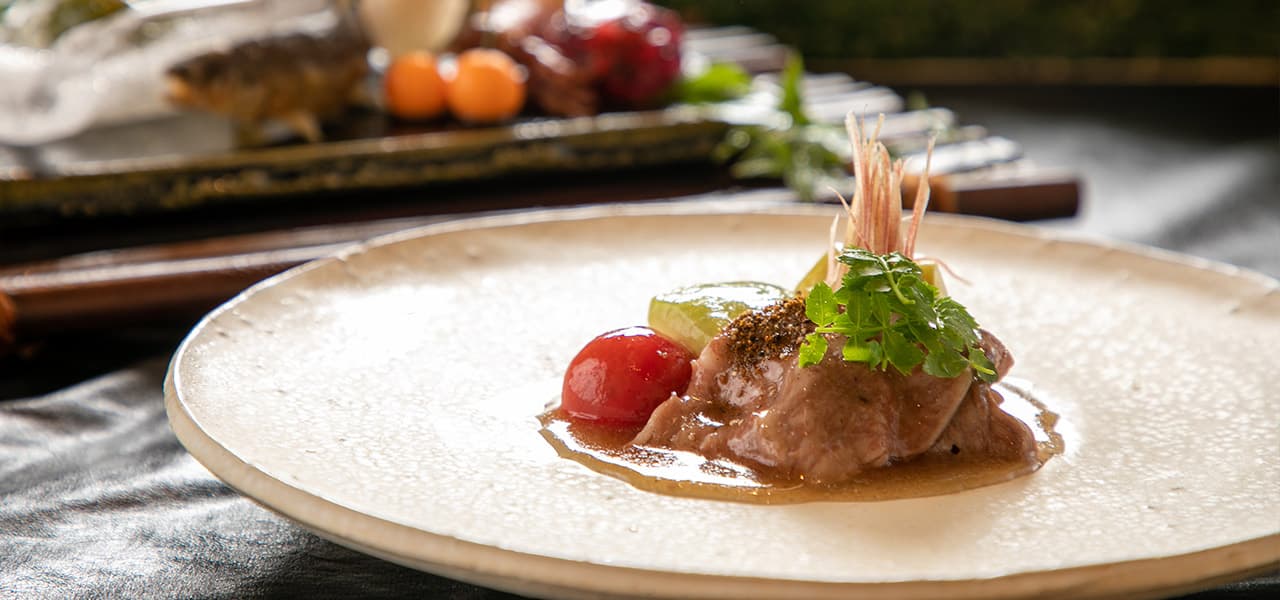 Close-up of a plated kaiseki course of simmered beef with garnish on a textured ceramic plate, Oyado Den Rikyu