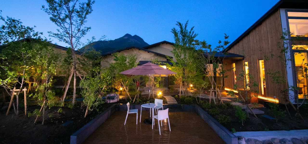 Landscaped courtyard garden with seating and Mt. Yufu silhouetted at blue hour, Oyado Den Rikyu Yufuin