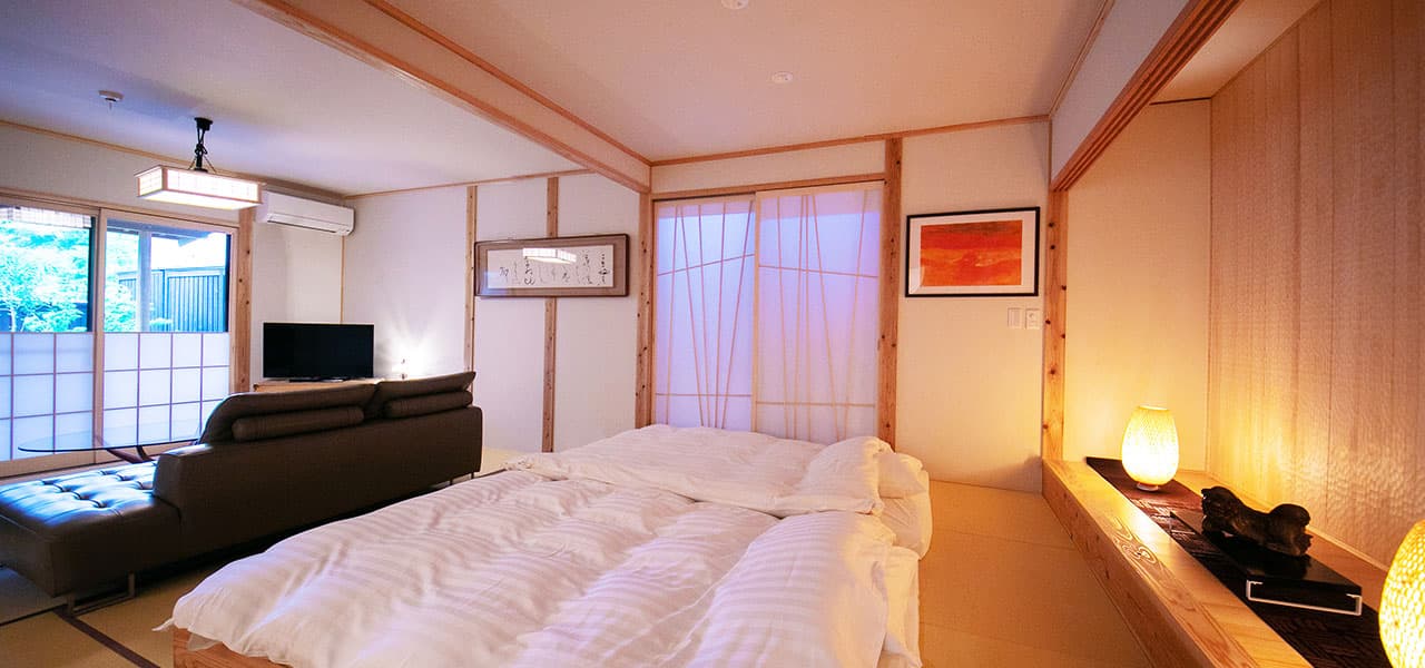 Spacious tatami guest room with futon bedding laid out and a paper-screen window at Oyado Den Rikyu