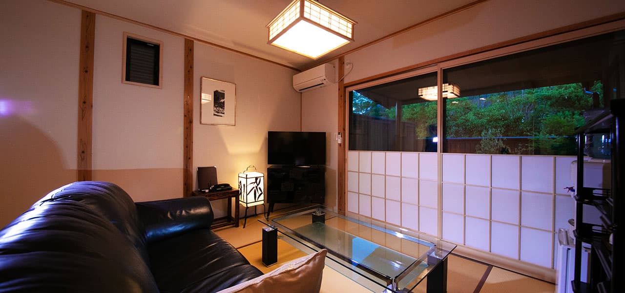 Guest room living area with leather sofa and shoji windows opening onto a green garden, Oyado Den Rikyu