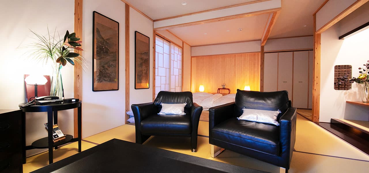 Japanese-style guest room with low bed, leather armchairs and ink-wash scroll art at Oyado Den Rikyu