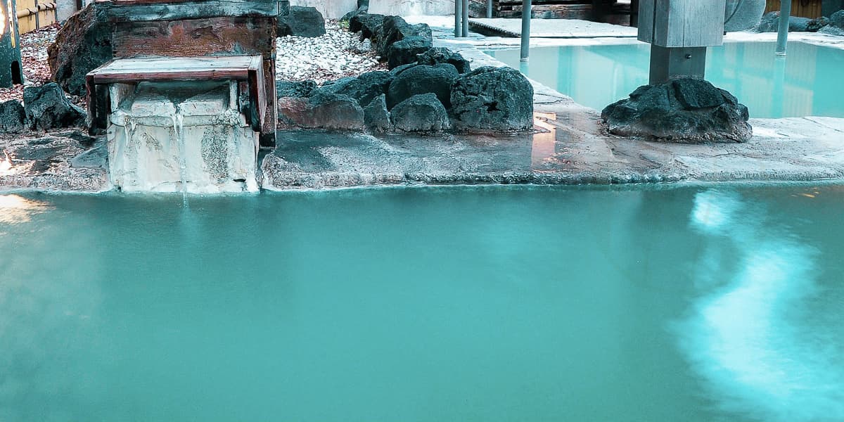 Indoor sulfur hot-spring bath with turquoise milky water and wooden cooling box at Yumoto Itaya