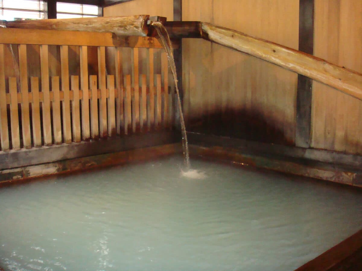 Wooden indoor bath at Yusaya Ryokan with milky alkaline Unagi-yu hot spring water pouring from a wooden spout