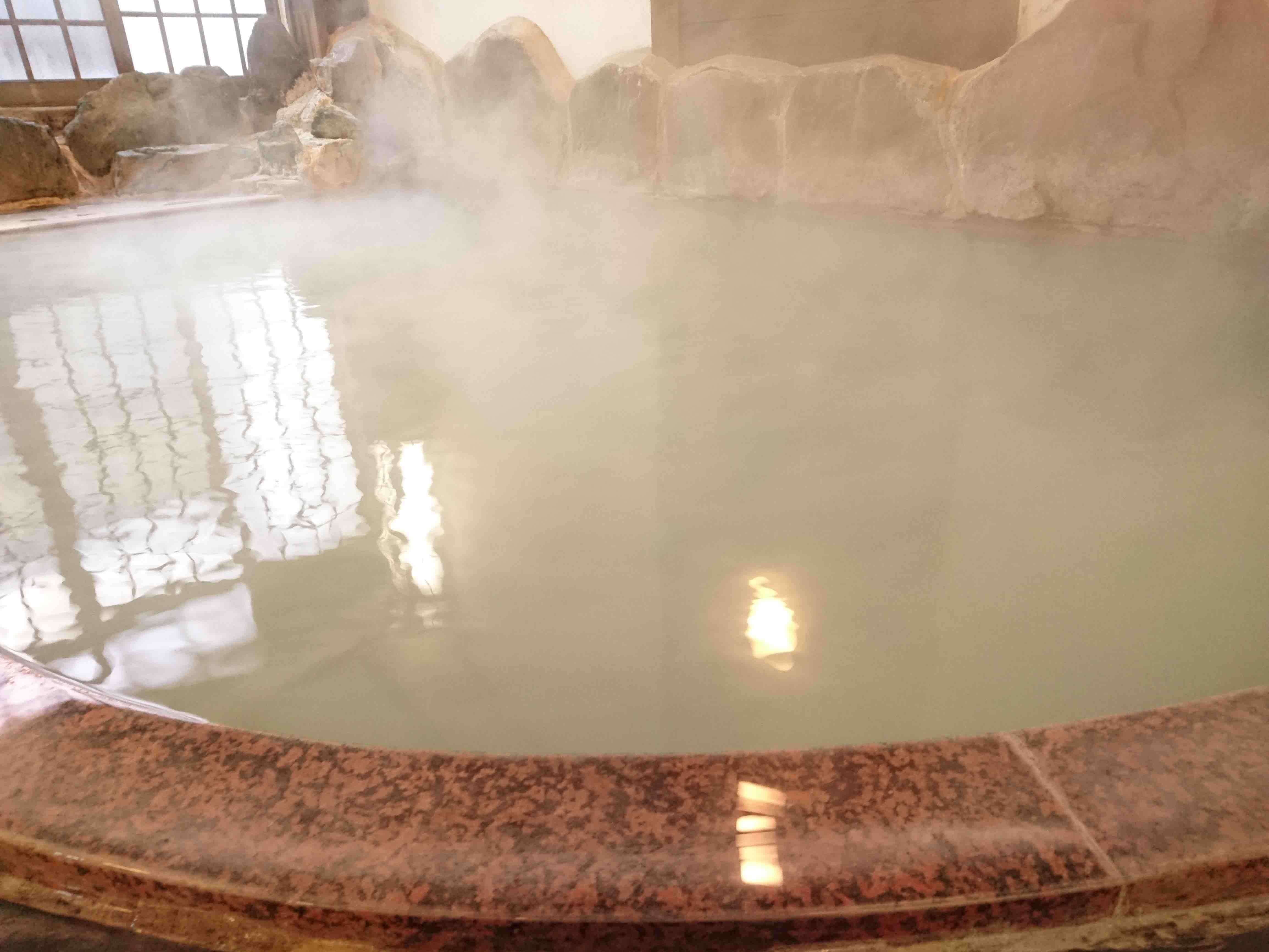 Indoor stone hot spring bath at Yusaya Ryokan with natural rock surround and rising steam, Naruko Onsen