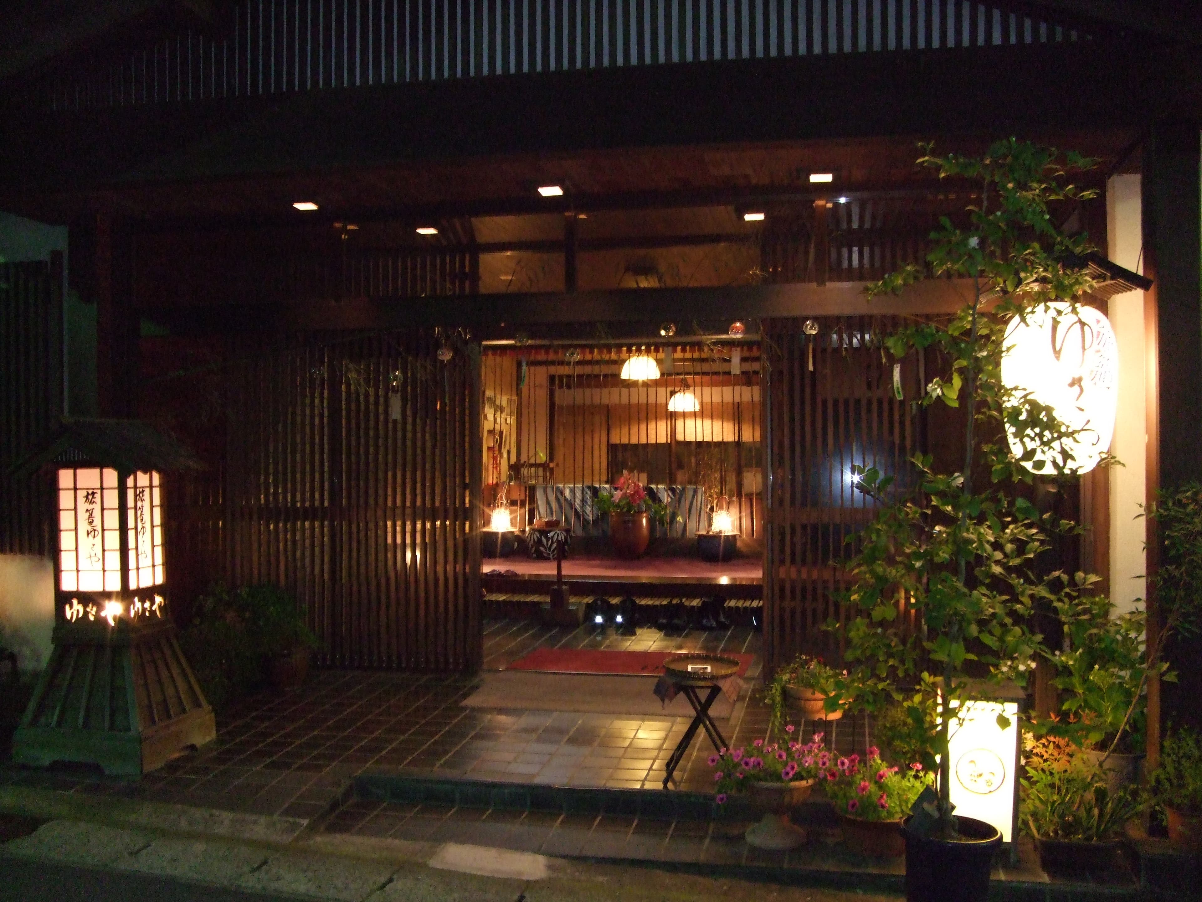 Warmly lit genkan entrance and tatami lounge of Yusaya Ryokan glowing at dusk with lanterns and potted flowers