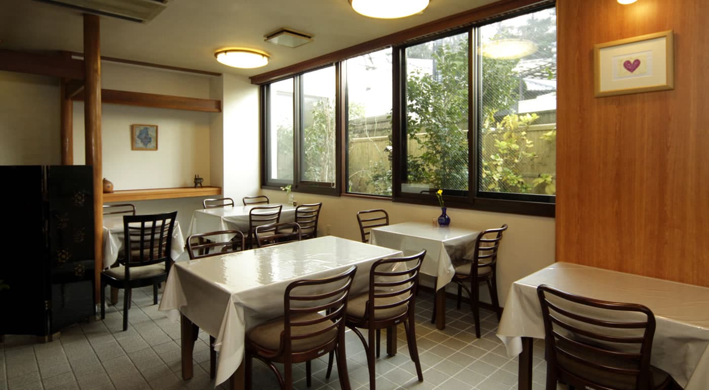 Bright Western-style dining room with white-clothed tables overlooking a small garden at Yamaichi Bekkan, Miyajima
