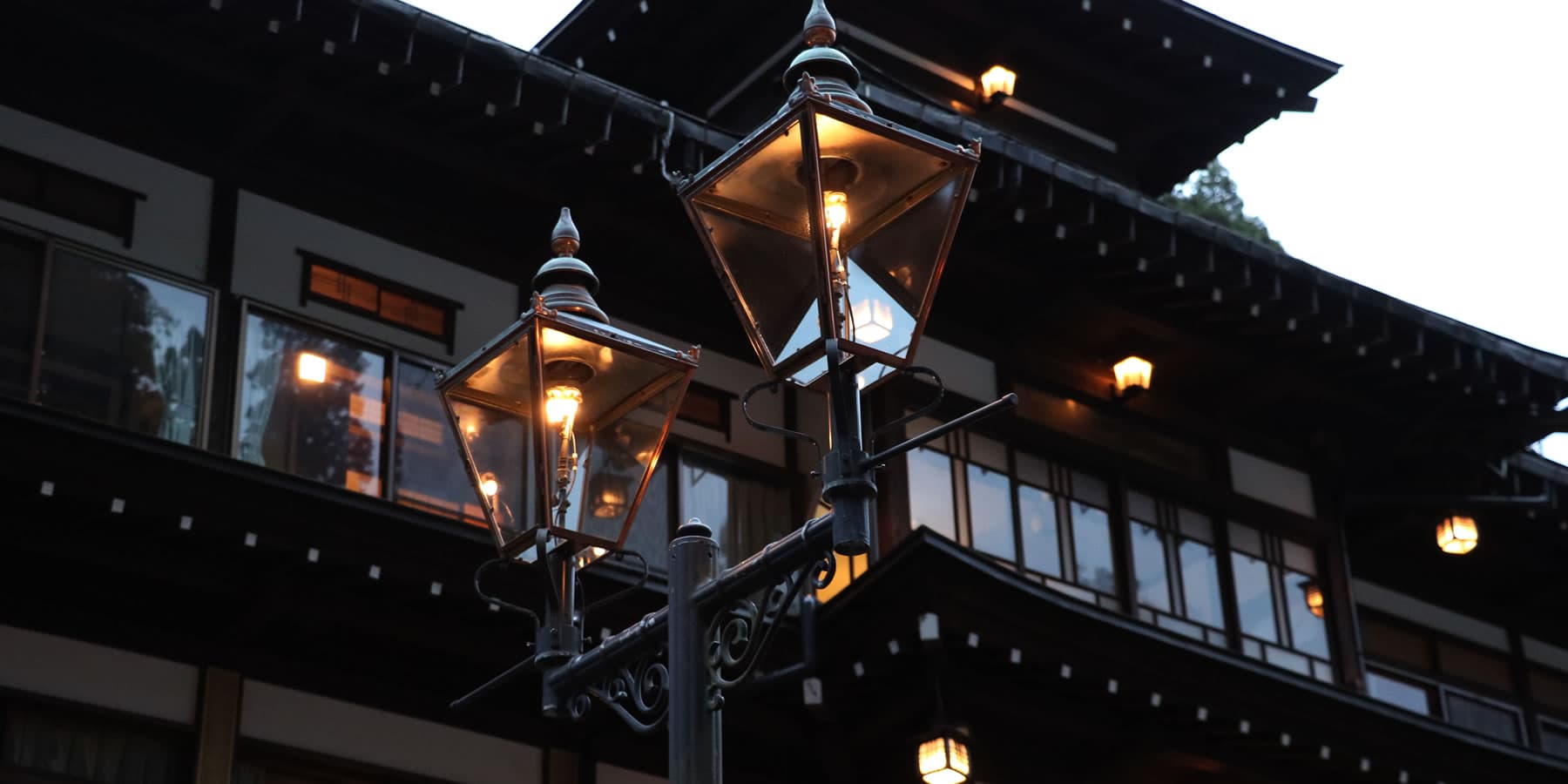 Vintage copper gas lamps glowing against Yanadaya's Taisho-era timber facade at dusk in Ginzan Onsen