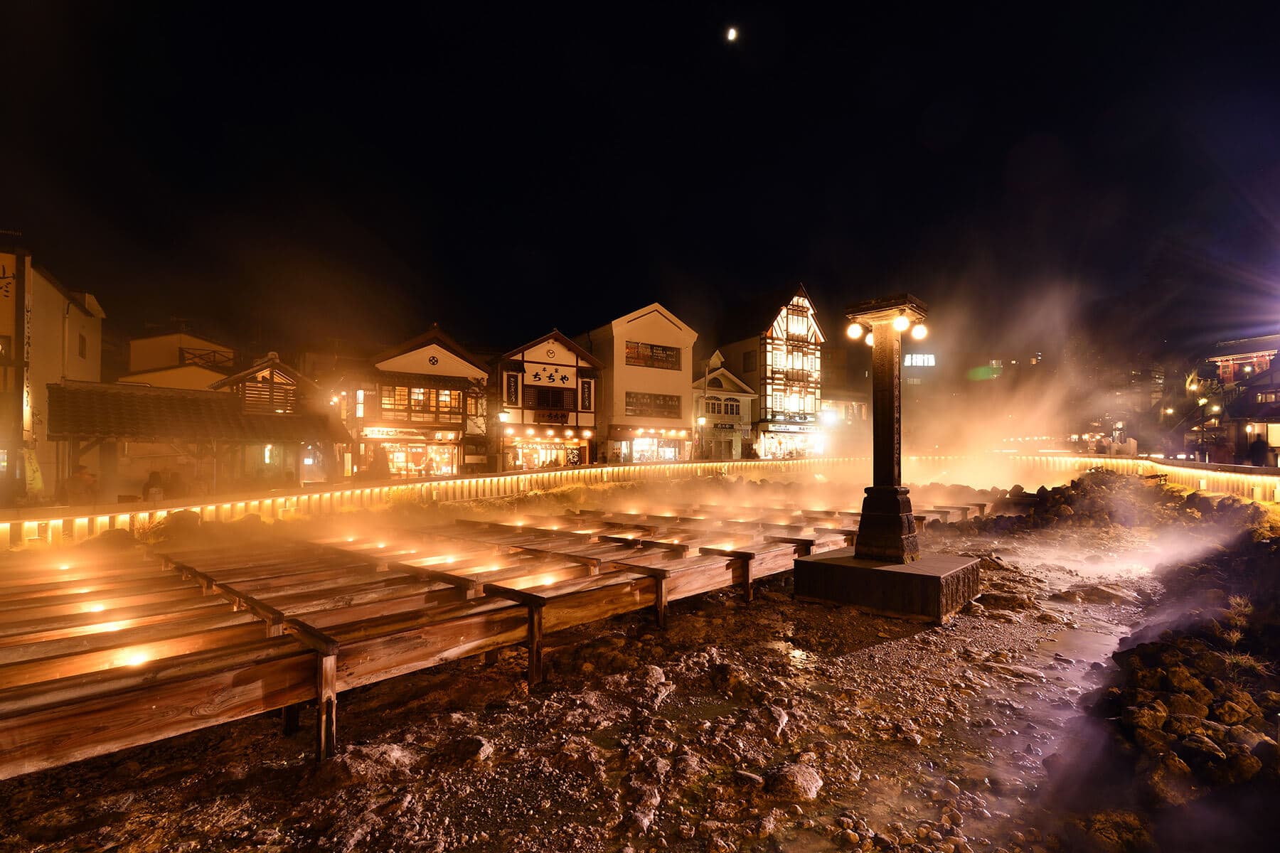 Kusatsu Yubatake hot-spring field glowing at night with rising steam and lantern-lit wooden buildings