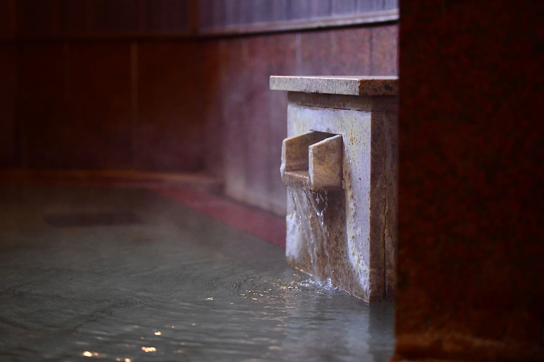 Indoor hot-spring bath with mineral water flowing from a stone spout into a warm pool