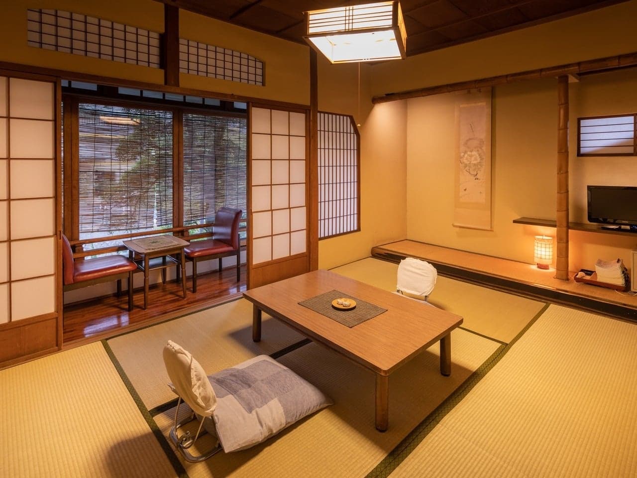 Traditional tatami guest room with low table, hanging scroll and window chairs at Yumoto Tamaikan ryokan