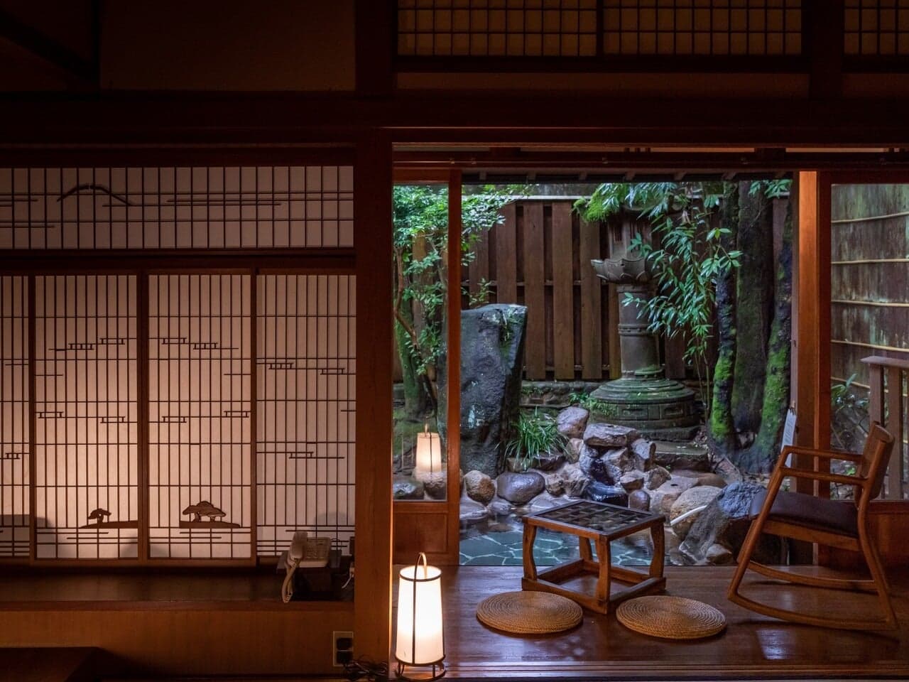 Tatami sitting room glowing with lantern light beside a mossy stone-lantern garden at Yumoto Tamaikan