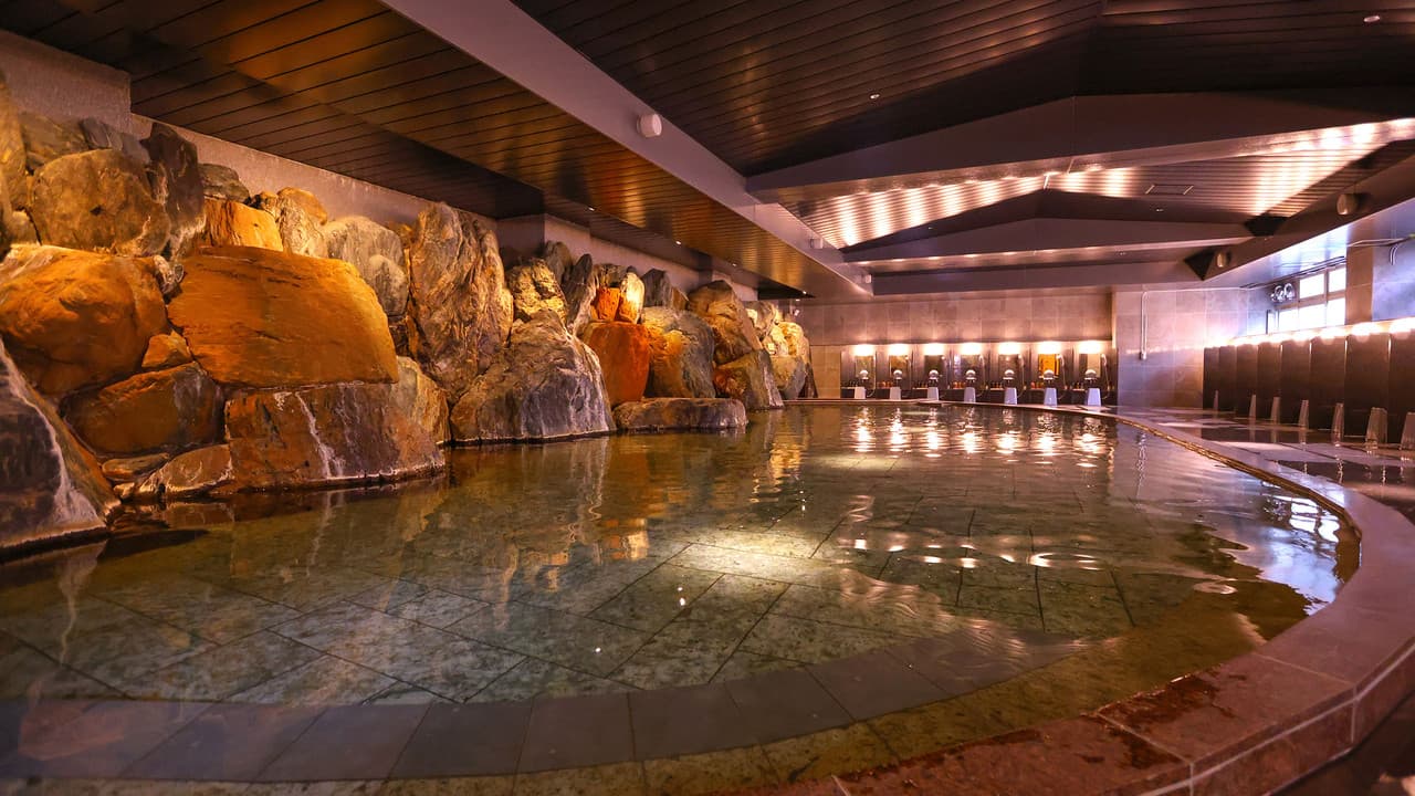 Large indoor rock hot-spring bath under a wood-beamed ceiling