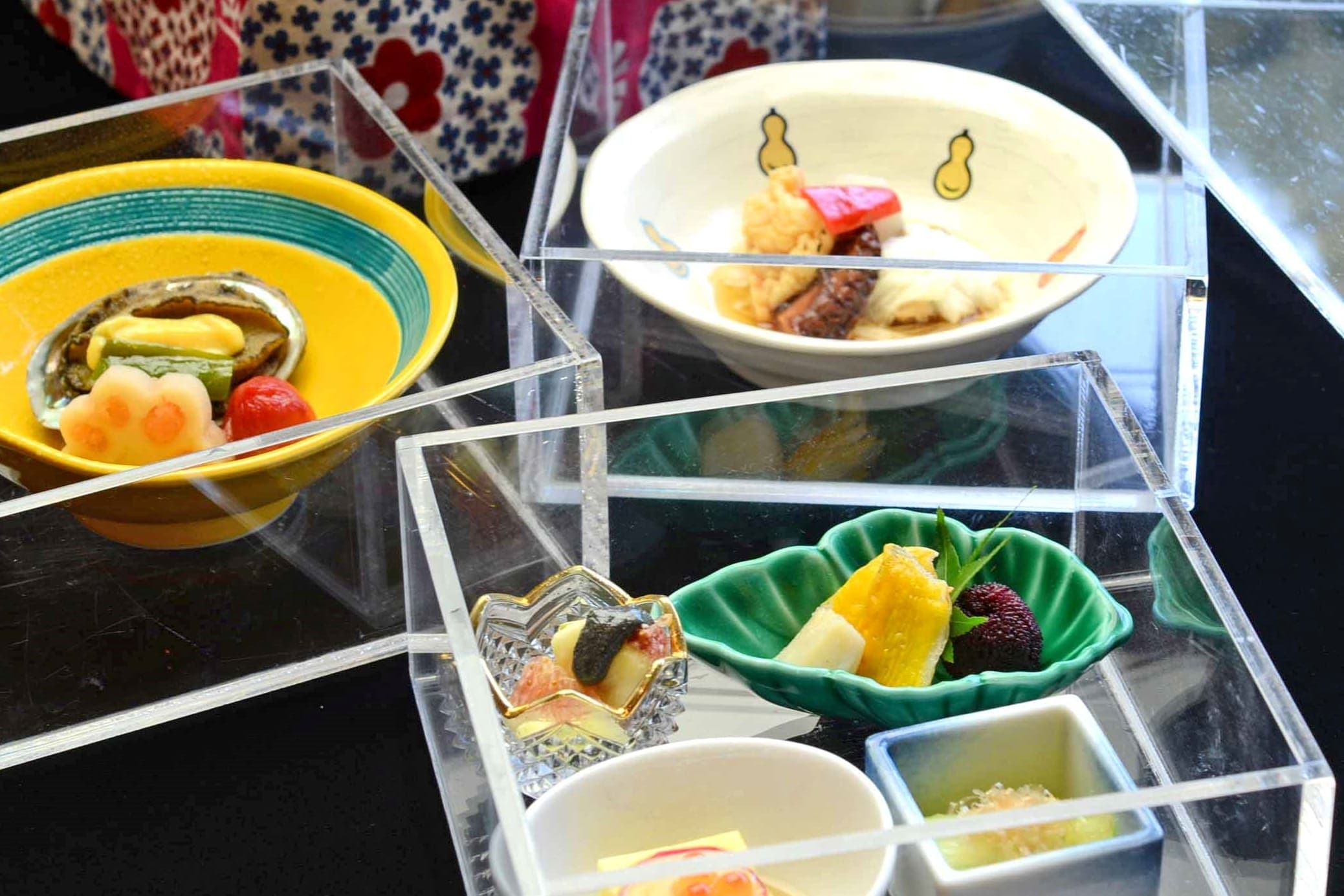 Hatago kaiseki assorted appetizers presented in stacked clear acrylic boxes with small ceramic dishes